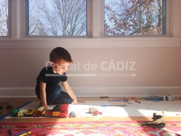 young toddler boy kneeling down and playing with toy cars in a sunny room with windows t20 jazx24