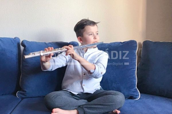 a 8years old boy sitting on the sofa playing classic music on a flute daytime sun reflection on the t20 42yzpr